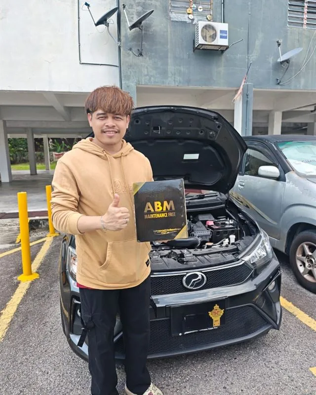 Customer giving a thumbs up beside their Perodua Bezza, holding the ABM Maintenance Free battery box