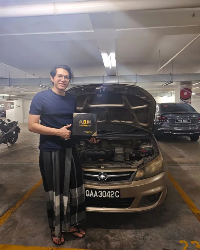 Customer holding an ABM Maintenance Free battery box beside their Proton Saga in a basement car park