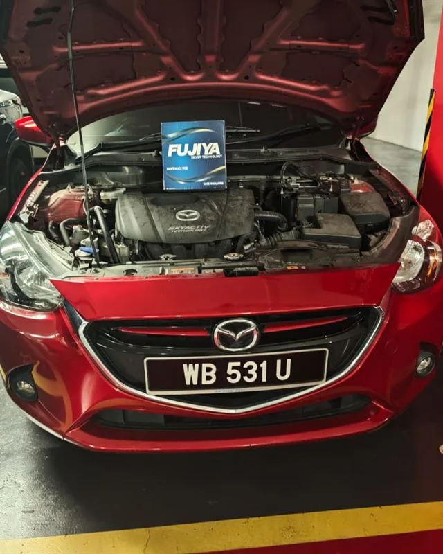 Red Mazda 2 in a basement car park bay with the bonnet open and a Fujiya Silver battery box on the engine