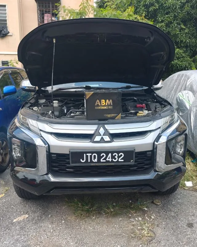 Mitsubishi Triton pickup parked at home with the bonnet open and an ABM Maintenance Free battery box on the engine