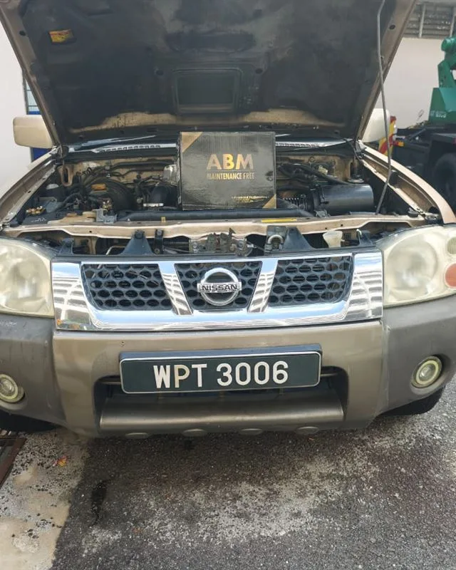 Gold Nissan Frontier pickup with the bonnet open and an ABM Maintenance Free battery box on the engine