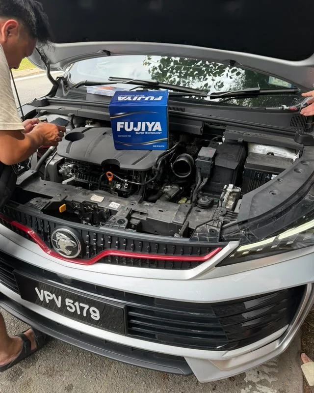 Technician working on a silver Proton X70 with a Fujiya Silver battery box resting on the engine bay