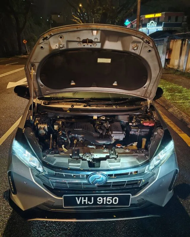 Silver Perodua Myvi stopped on a public road at night with the bonnet open during an on-site battery replacement