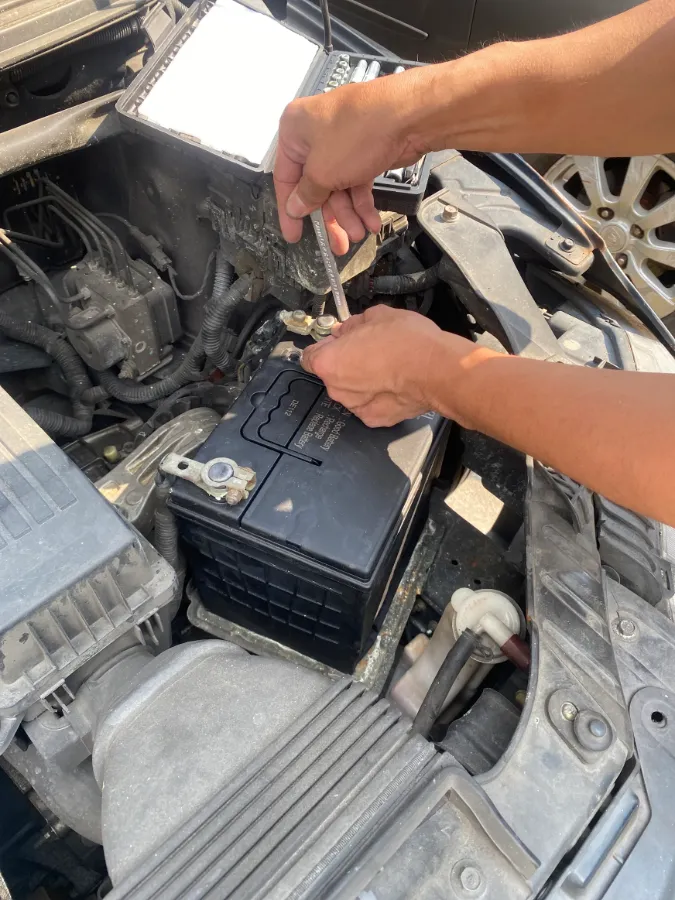 Technician tightening a car battery terminal with a spanner during an on-site replacement