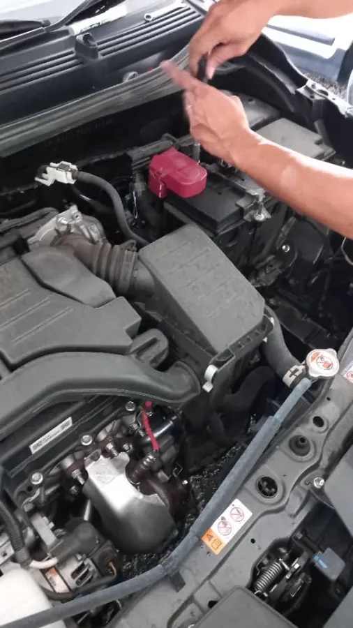 Technician working above a car battery with a red terminal cover in an engine bay