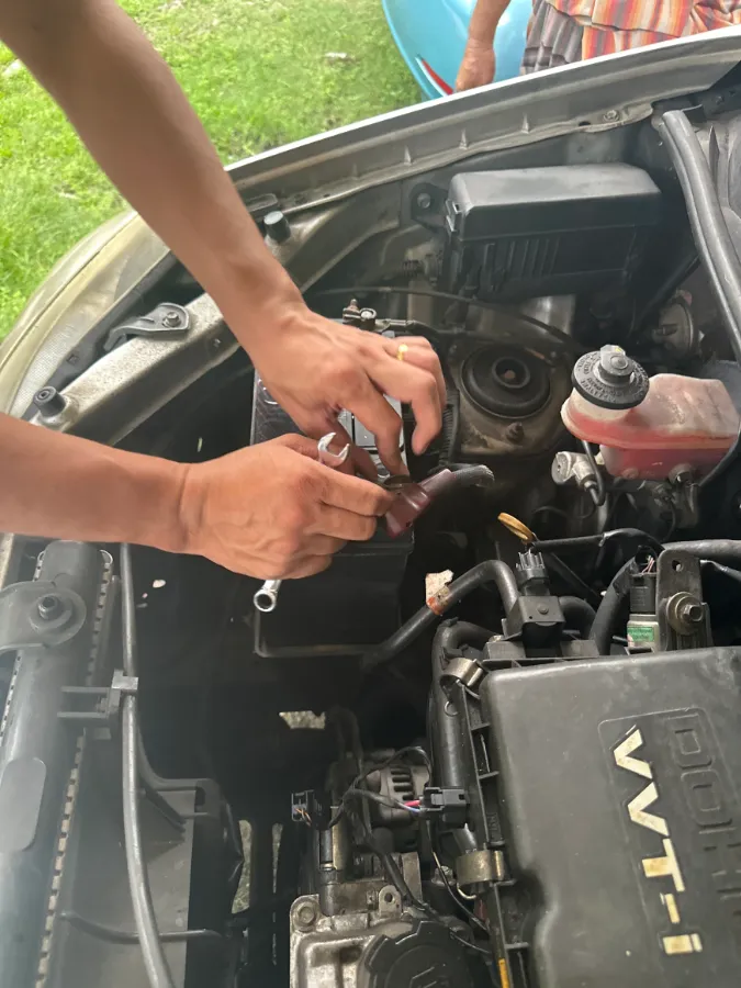 Technician fitting a car battery terminal on a car parked on grass