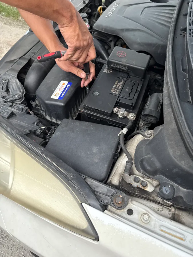 Technician using a screwdriver on a newly fitted 12V car battery in an engine bay