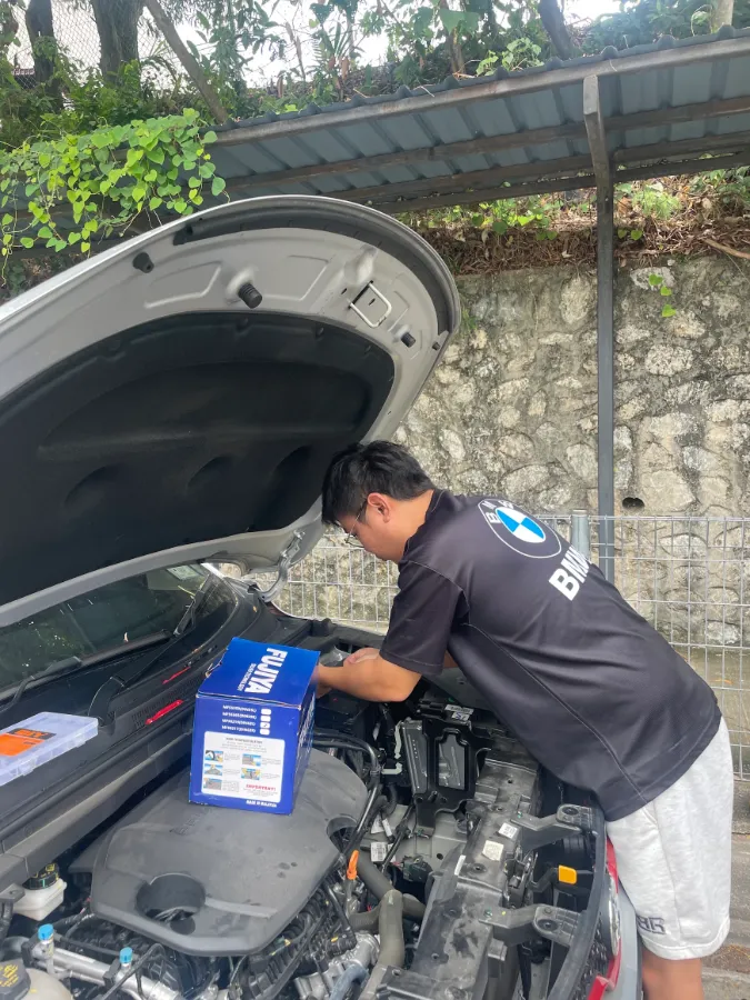 Technician placing a new Fujiya car battery box on the engine bay of a white car