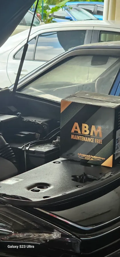 ABM Maintenance Free car battery box resting on the open bonnet of a car