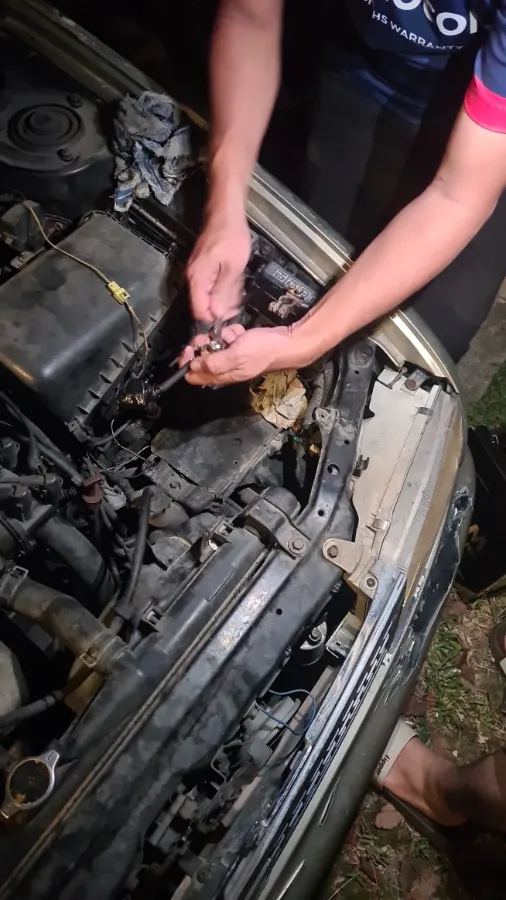 Technician working on a car battery terminal by torchlight during a night call-out