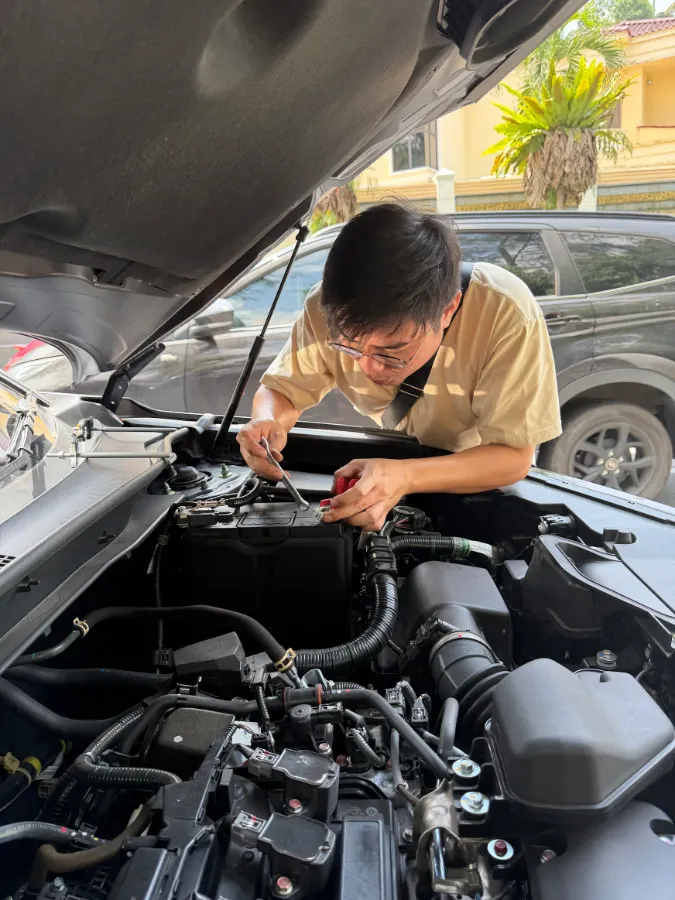 Technician fitting a new car battery in the engine bay of a car on a residential driveway
